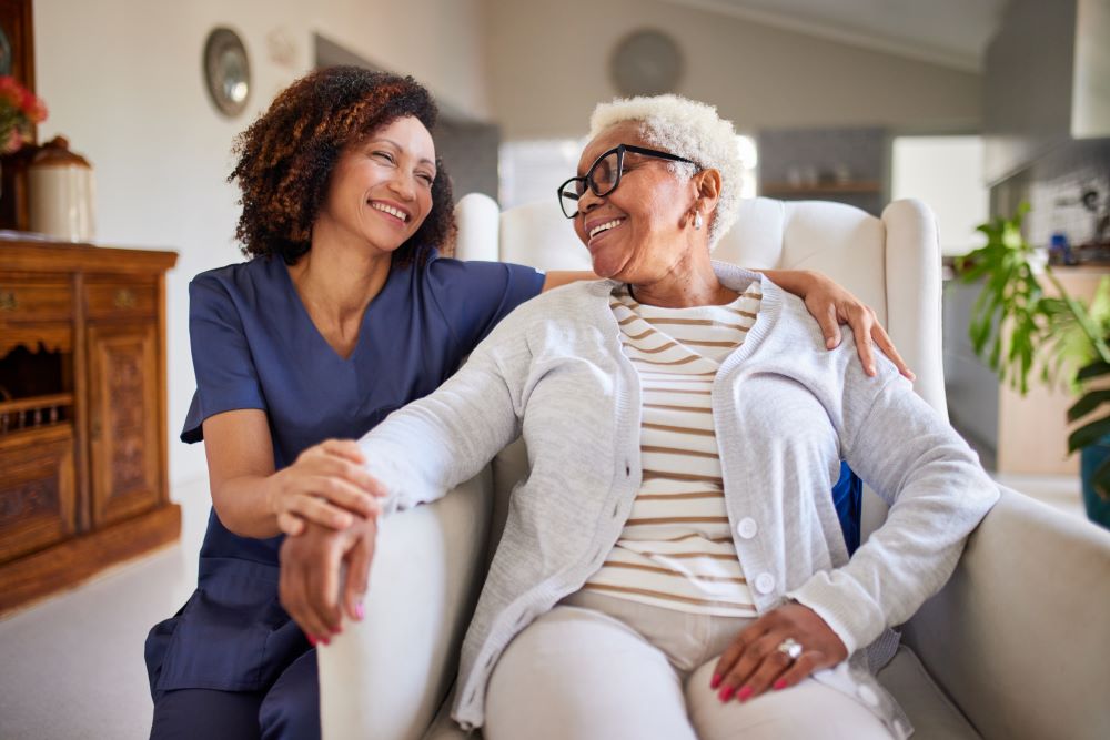 Smiling caregiver and elderly woman sitting together in Houston, TX